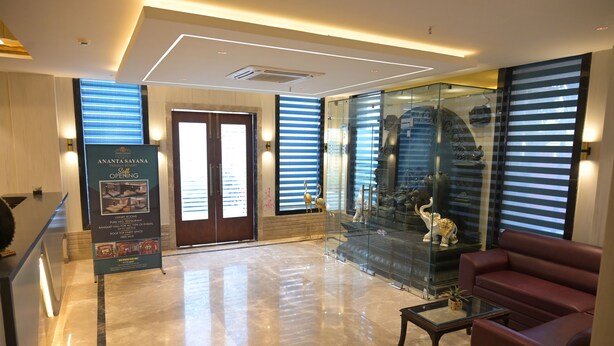 A lobby with a reception desk, a glass display case with decorative items, a red sofa, and a polished marble floor. - Hotel Ananta Sayana  (Bhubaneshwar)