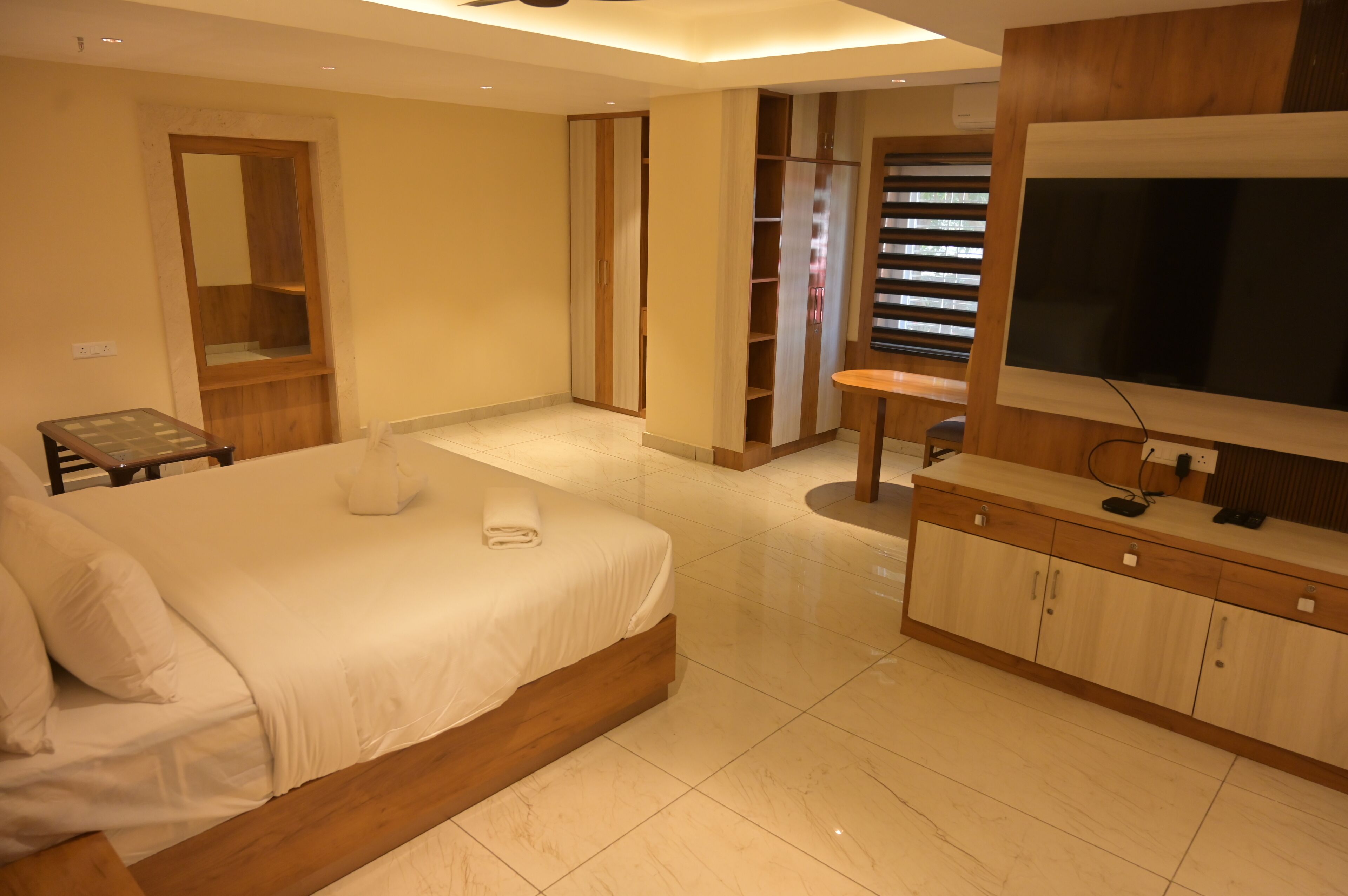 Une chambre avec un grand lit, une télévision, une armoire en bois et une petite table.