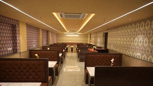 A restaurant with booths and tables, patterned wallpaper, and a central walkway. - Hotel Ananta Sayana  (Bhubaneshwar)