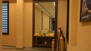 A hallway with a mirror reflecting a room, a window with blinds, and decorative golden vases on a shelf. - Hotel Ananta Sayana  (Bhubaneshwar)
