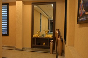 Um corredor com um espelho refletindo um quarto, uma janela com persianas e vasos dourados decorativos em uma estante.