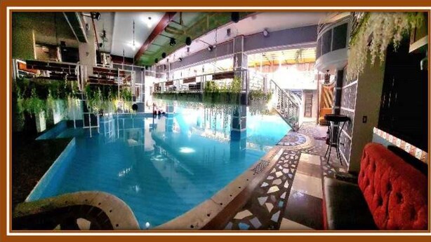 Una piscina interior con suelo de baldosas, rodeada por un balcón con barandillas y un sofá rojo.