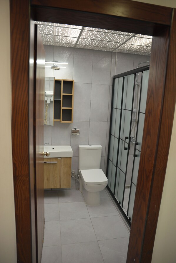 A bathroom with a wooden cabinet, a white toilet, and a glass shower enclosure. - Nahita Otel (Nigde)
