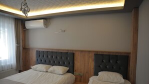 A hotel room with two beds, a wooden headboard, a ceiling light, and an air conditioning unit.
