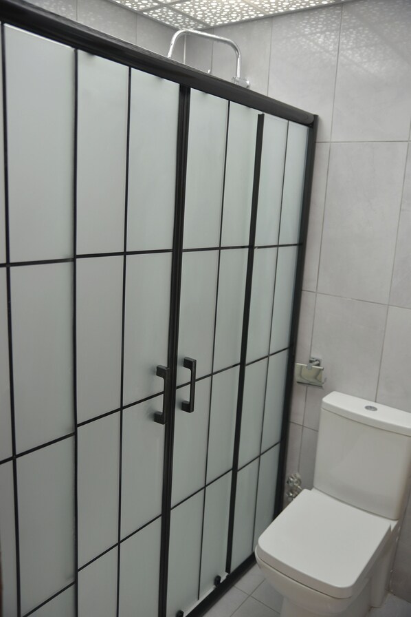 A bathroom with a white toilet and a glass-enclosed shower stall. - Nahita Otel (Nigde)