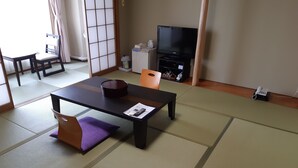 Een kamer met tatami vloermatten, een lage tafel met kussen, een televisie en een telefoon.