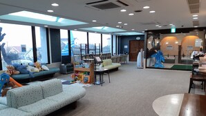Een ruime lobby met een grote zithoek, een speelruimte voor kinderen en een receptiebalie.