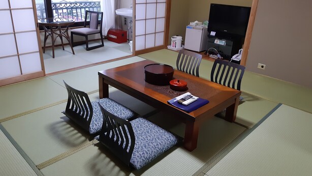 Een traditionele Japanse kamer met tatami vloeren, een houten eettafel met kussens en een televisie.