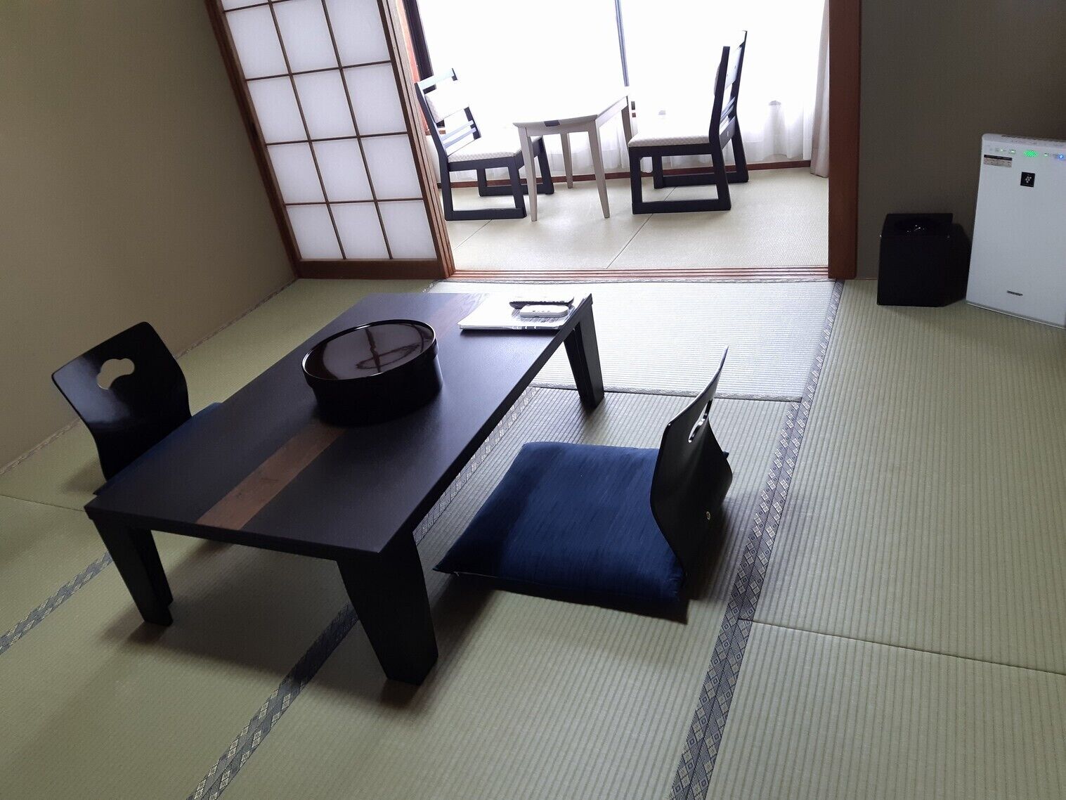 Een kamer met tatami matten, een lage tafel, twee stoelen, een klein tafeltje met een kopje en een schuifdeur.