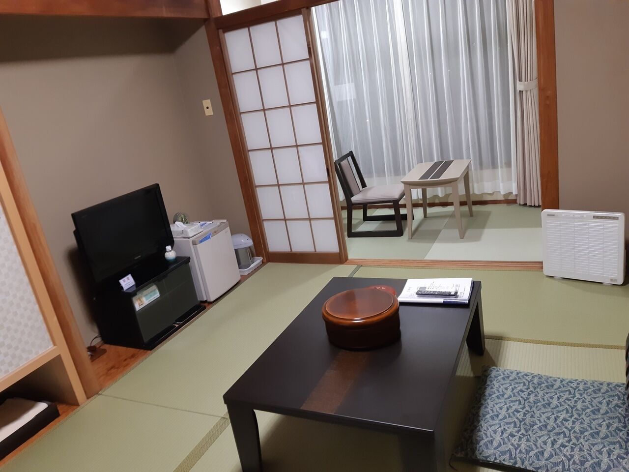 Een traditionele Japanse kamer met tatami vloeren, een lage tafel met een kom, een televisie en een futonbed.