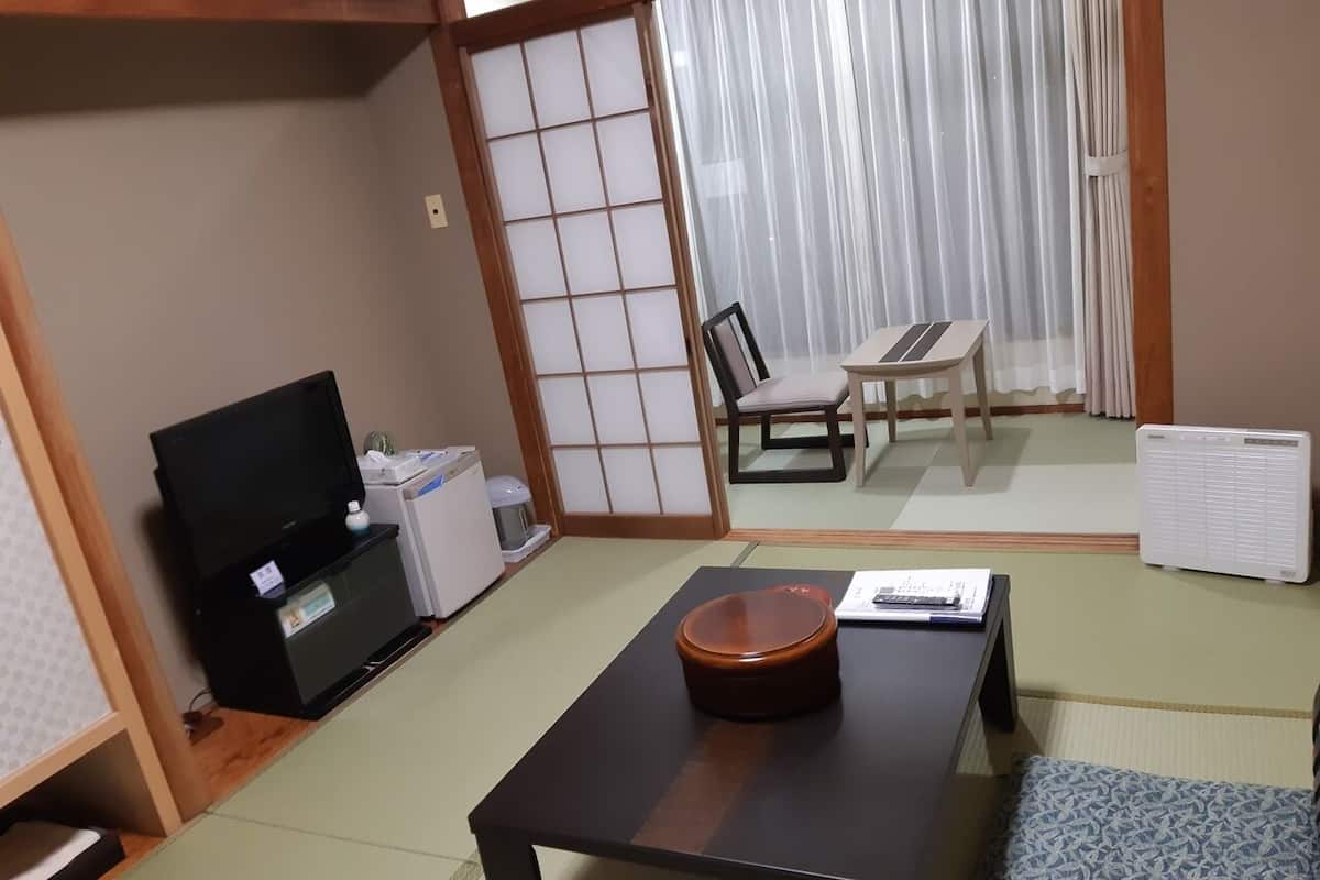 Ein traditioneller japanischer Raum mit Tatami-Bodenbelag, einem niedrigen Tisch mit einer Schale, einem Fernseher und einem Futon-Bett.