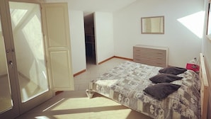 A bedroom with a skylight, a bed with a patterned bedspread, a dresser, and a mirror on the wall.