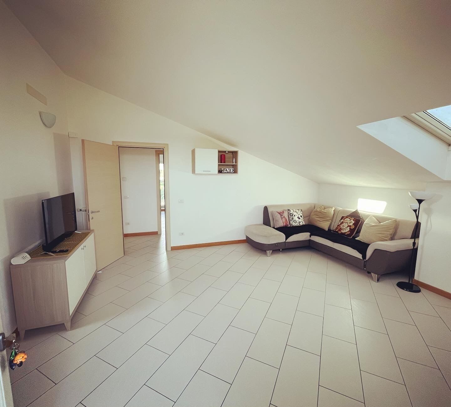 A spacious living area with a large L-shaped sofa, a flat-screen TV, and a ceiling fan.