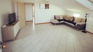 A spacious living area with a large L-shaped sofa, a flat-screen TV, and a ceiling fan.