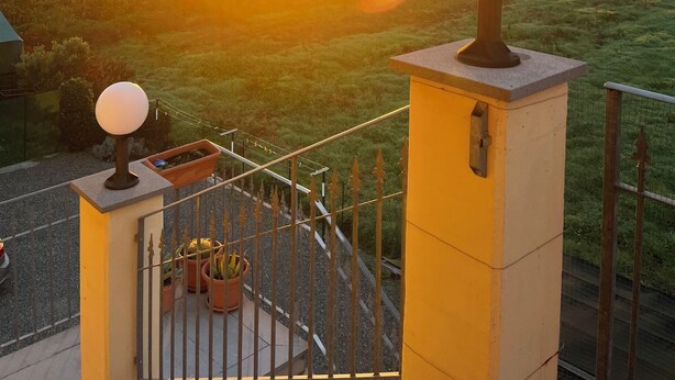 A balcony with a view of a sunset over a field, a lamp post, and a potted plant.