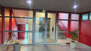 A modern lobby with a glass entrance, red walls, and a staircase.