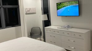 A bedroom with a bed, a desk, a chair, a TV, and a ceiling fan.