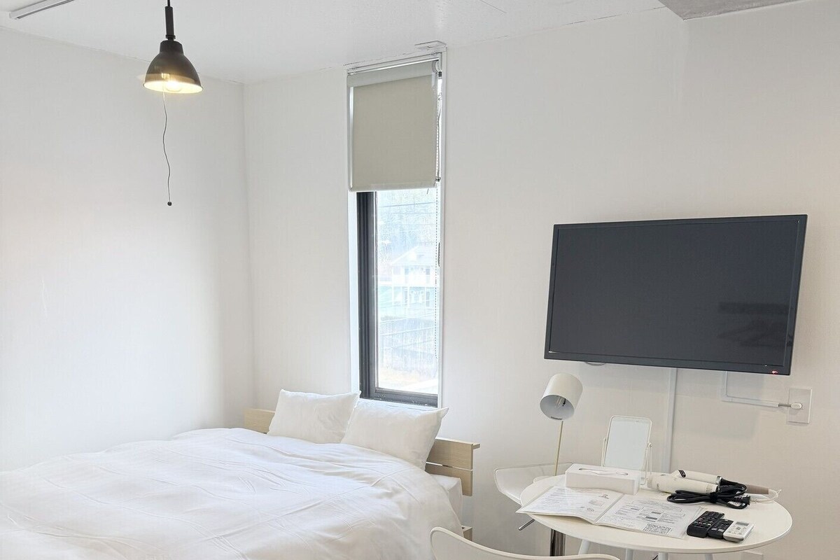 Une chambre avec un lit, un bureau et une chaise, une télévision et une fenêtre.