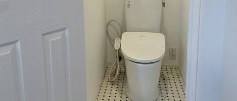 A bathroom with a toilet, a hand dryer, and a small sign on the wall.