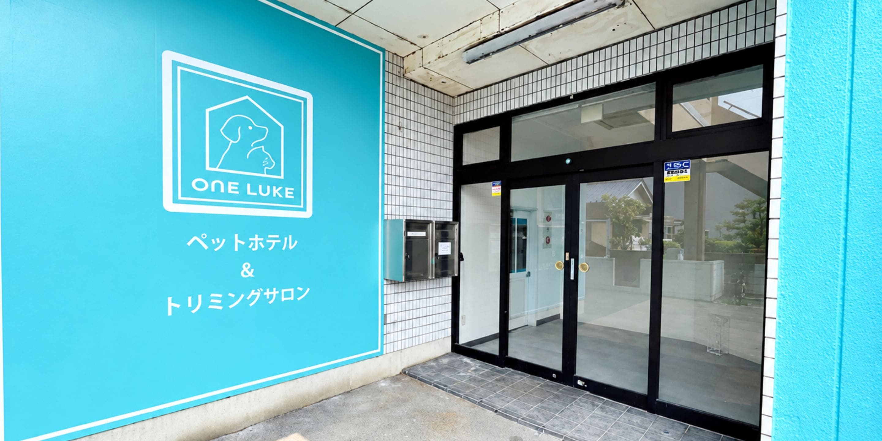 A building entrance with a blue sign featuring a dog icon and Japanese text, indicating a pet-friendly establishment.