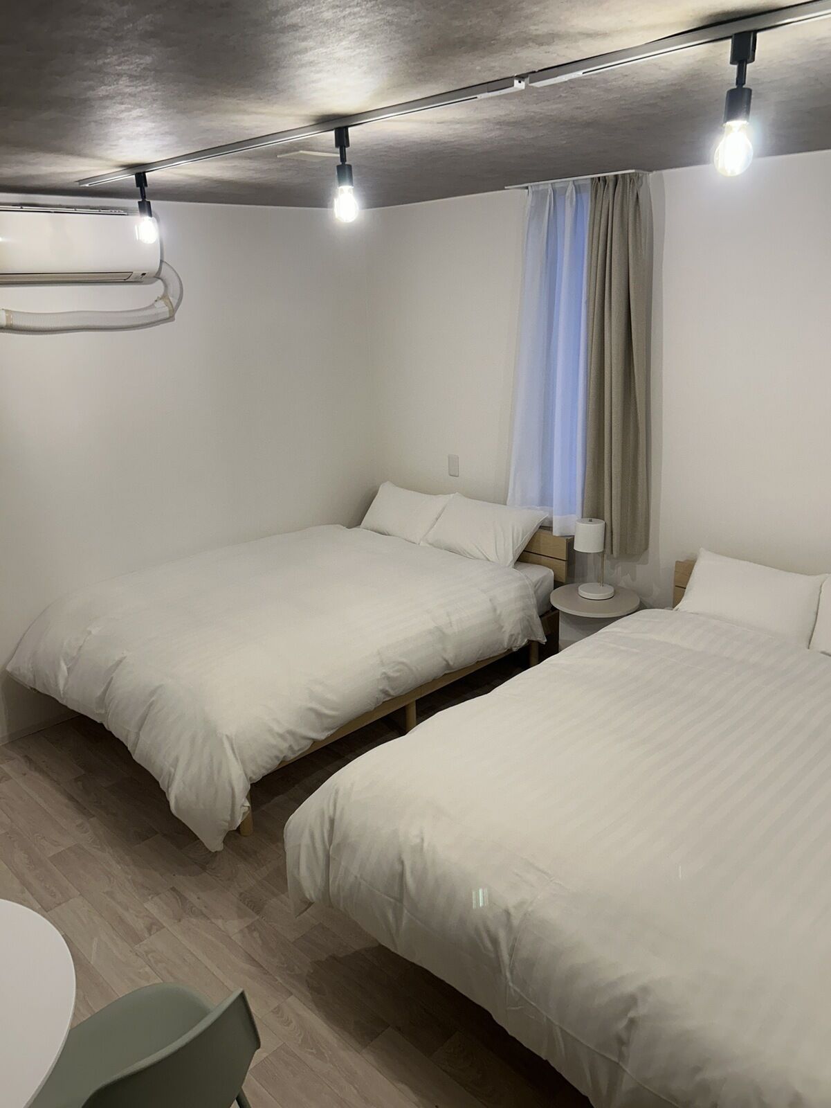 Ein Hotelzimmer mit zwei Betten, einem runden Tisch und einer Decken-Klimaanlage.