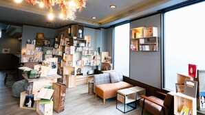 A cozy reading nook with a plush sofa, a small wooden table, and a bookshelf filled with books and decorative items. - The Book Lounge Hotel Kani (Kani)