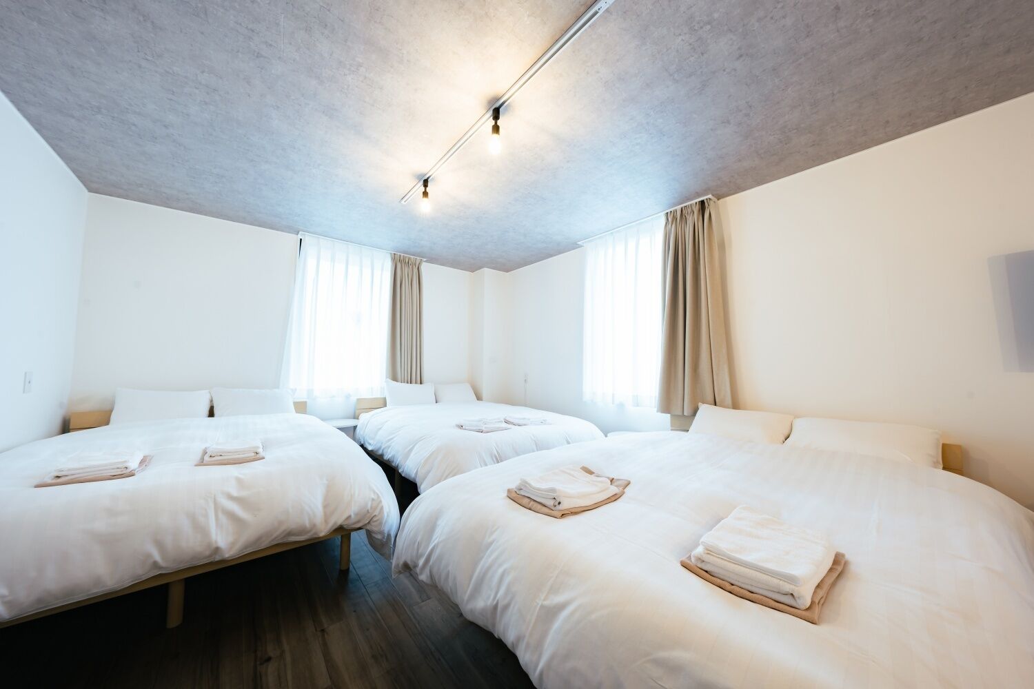 A hotel room with two single beds, a wooden floor, and a ceiling with recessed lighting.