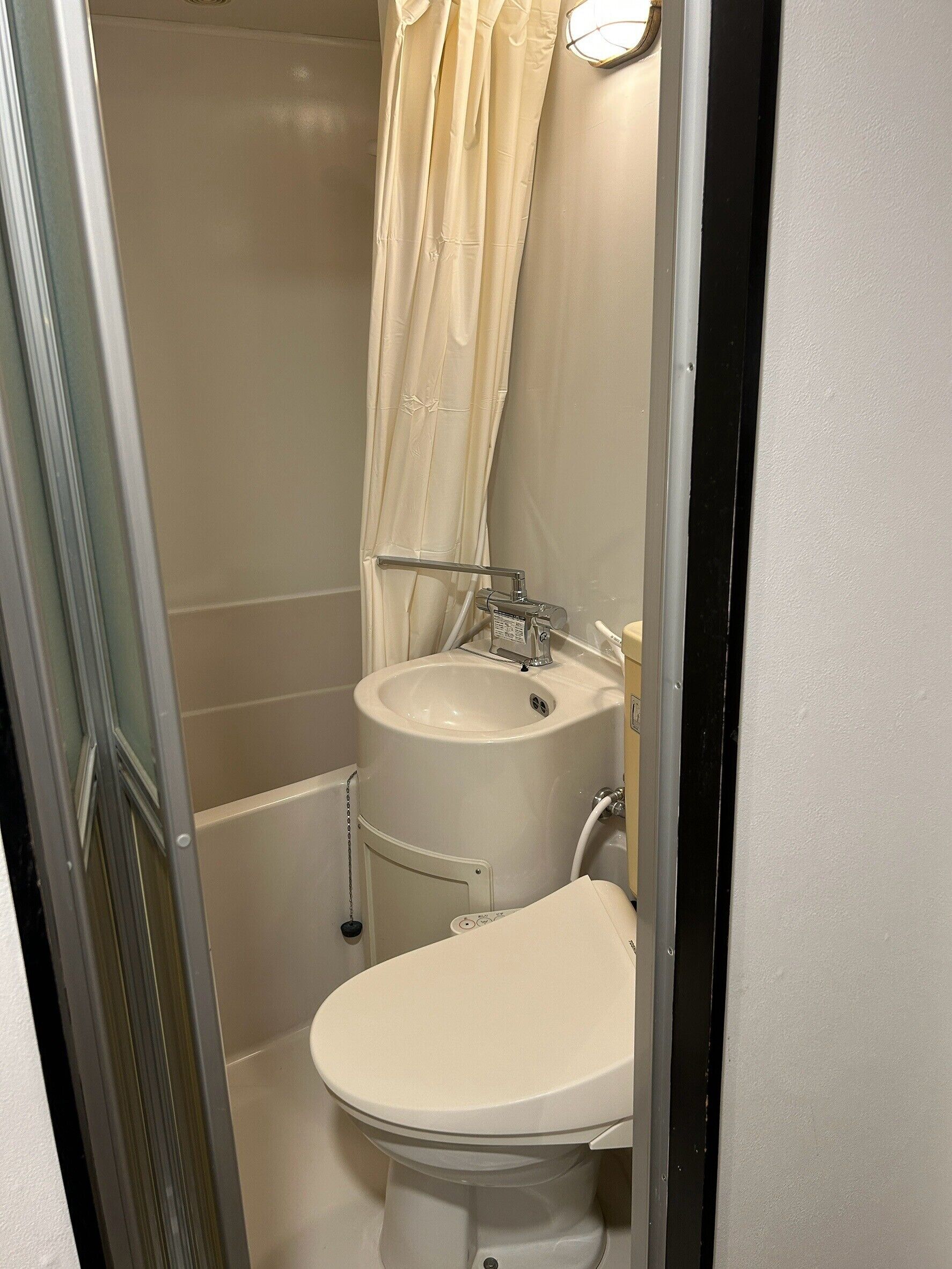 A small, compact bathroom with a toilet, sink, and shower area.