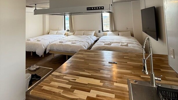 A modern hotel room with a kitchenette, three beds, a wooden dining table, and a large window. - The Book Lounge Hotel Kani (Kani)