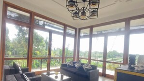 Una habitación amplia con ventanas grandes, muebles de mimbre y una lámpara de techo.