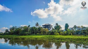 Paisaje tropical con un cuerpo de agua que refleja el cielo, rodeado de exuberante vegetación y una estructura de edificio destacada.