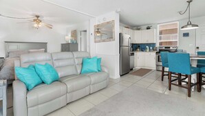 A modern living room with a grey sofa, teal cushions, and a dining area with blue chairs. - Gorgeous Beach and Tennis Condo 5608 (Bonita Springs)