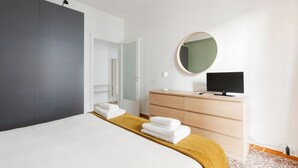 Une chambre d’hôtel moderne avec un grand lit, une commode en bois, un téléviseur à écran plat et un grand miroir rond accroché au mur.