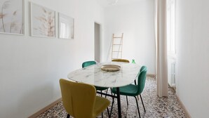 Un coin repas avec une table en marbre, des chaises vertes et jaunes, et des œuvres d’art encadrées accrochées au mur.