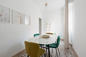 A dining area with a marble table, green and yellow chairs, and framed artwork on the wall. - GuestHost - San Siro Modern Apartment with Balcony (Milano)
