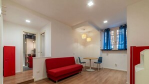 Una sala de estar moderna con un sofá rojo, dos sillones, una mesita redonda y una ventana con cortinas azules.
