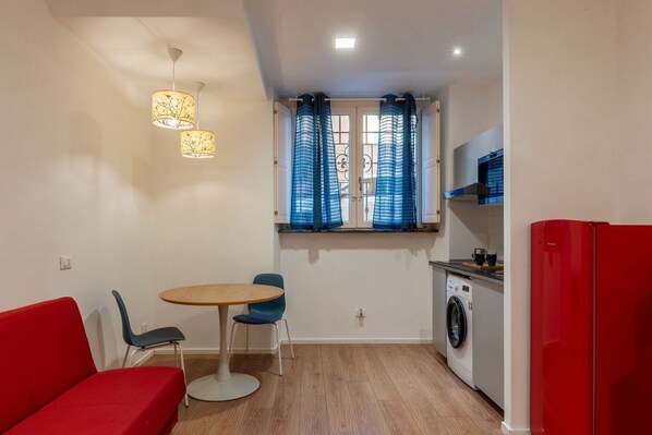 A compact living space with a dining area, a red sofa, a washing machine, and a red refrigerator.