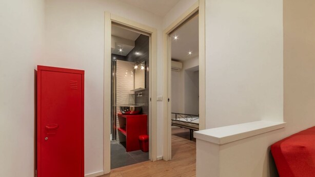 Un pasillo con un mueble de almacenamiento rojo, una pequeña kitchenette y una cama al fondo.