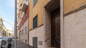 Una calle estrecha con coches aparcados y un edificio con un amplio acceso abierto.