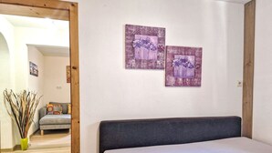 Une chambre à coucher avec un lit, un canapé gris et deux tableaux représentant des fleurs, accrochés au mur.