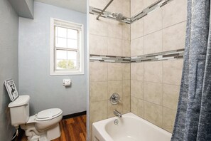Un baño con inodoro, ventana, ducha con pared de azulejos y bañera.