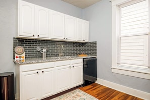 A kitchen with white cabinets, a black tiled backsplash, a dishwasher, and a window with blinds.