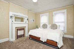 Quarto com cama, lareira e duas janelas.