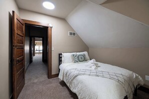 A bedroom with a bed, a wooden door, a hallway, and a sloped ceiling.