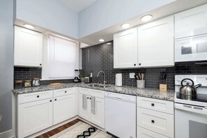 A modern kitchen with white cabinets, a granite countertop, a built-in oven, and a kettle.