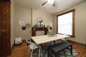 A dining area with a wooden table, white chairs, a black bench, a ceiling fan, and a window with blinds.