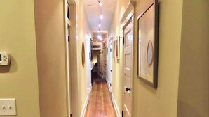 A narrow hallway with wooden flooring, white walls, and doors on both sides.