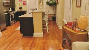 A modern kitchen with dark cabinets, a microwave, and a stove. There is a small island with a sink and a chair. The floor is wooden, and there is a plant in the corner.
