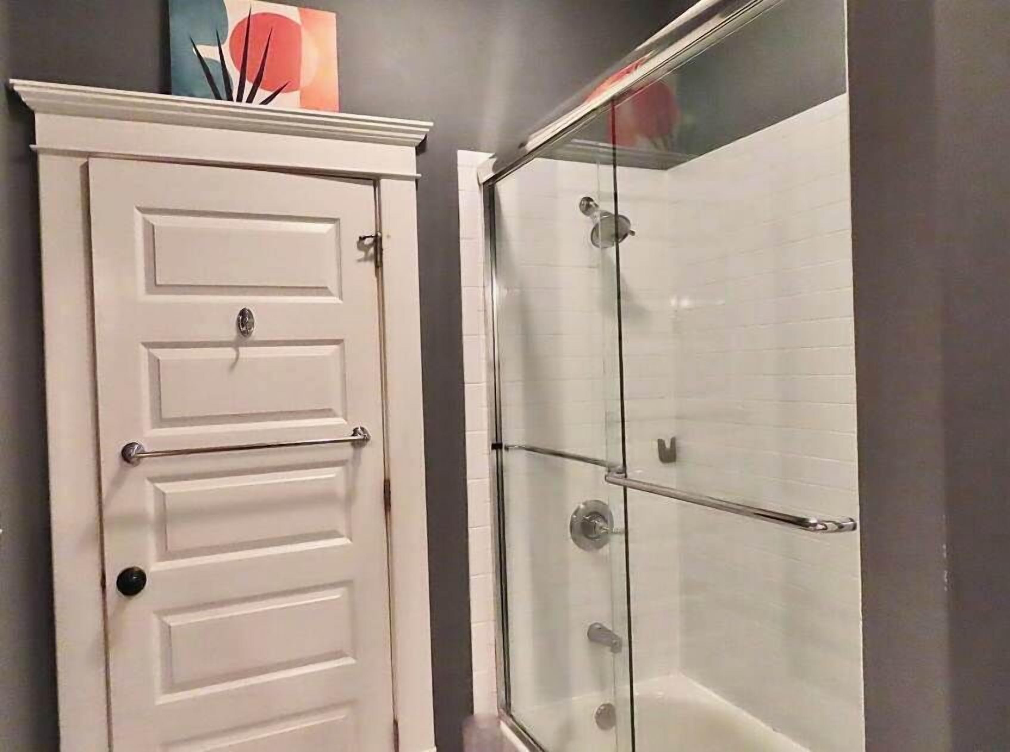 A bathroom with a white door, a glass shower enclosure, and a towel rack.