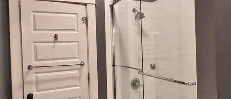 A bathroom with a white door, a glass shower enclosure, and a towel rack.